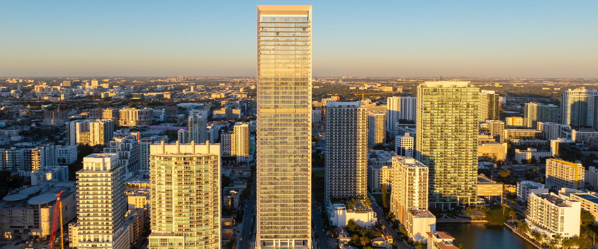 Aerial view of a tall, modern high-rise surrounded by smaller buildings.